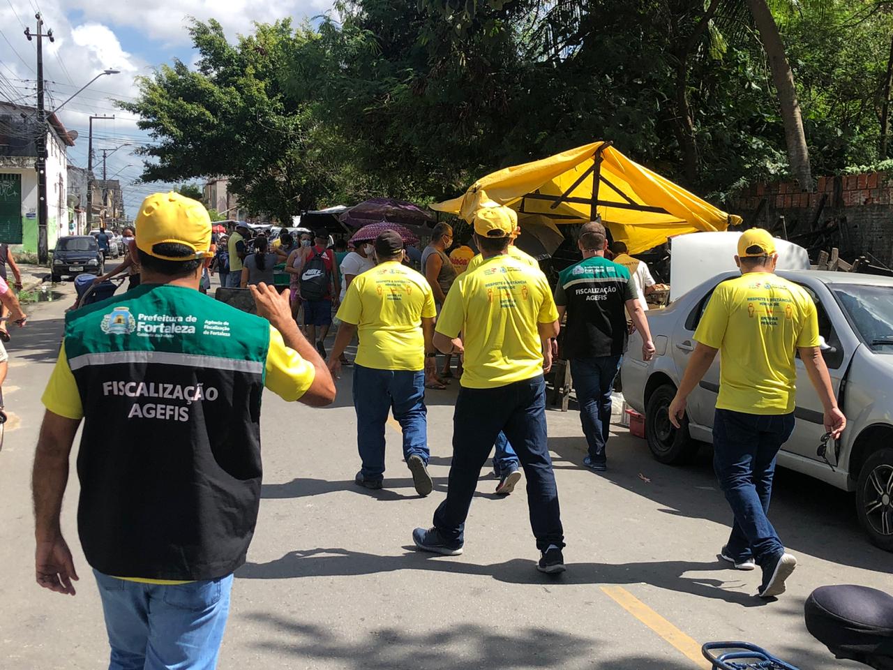 fiscais andando de colete em rua com barracas de feira